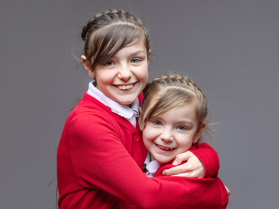 Two sisters in red school uniform — sibling school portrait